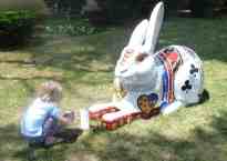 a five-year-old girl crouches to take a picture of a giant rabbit's feet.