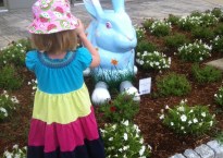 A young girl takes a picture of a giant blue rabbit.