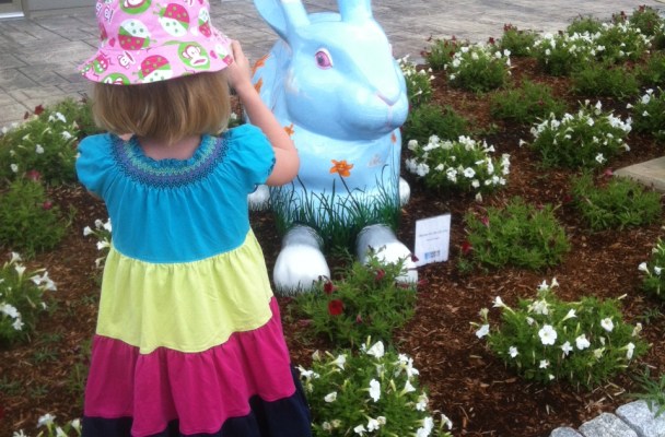 A young girl takes a picture of a giant blue rabbit.