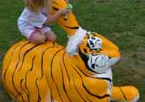 A five year old girl sits on the back of a giant tiger-striped rabbit, hugging its remaining ear. The other ear has been lopped off and a gauze bandage applied to its stump.