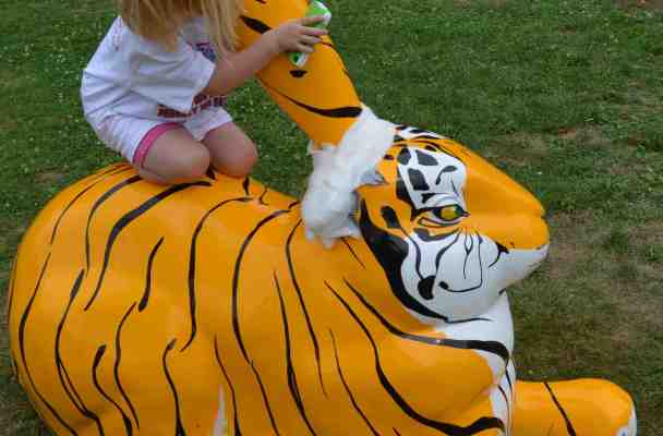 A five year old girl sits on the back of a giant tiger-striped rabbit, hugging its remaining ear. The other ear has been lopped off and a gauze bandage applied to its stump.