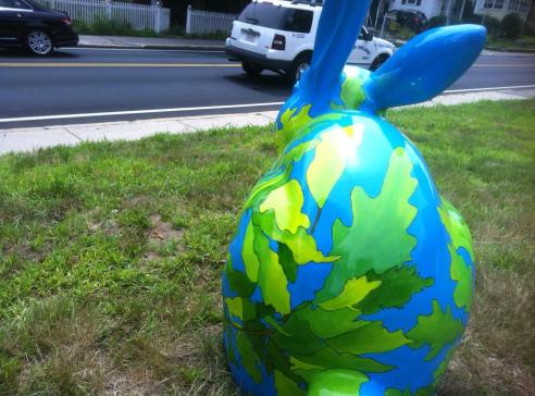 Avery Oak sits on a lawn. The blue bunny is covered with a network of oak tree branches, leaves, and acorns. 