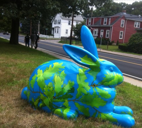 Avery Oak sits on a lawn. The blue bunny is covered with a network of oak tree branches, leaves, and acorns. 