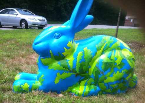 Avery Oak sits on a lawn. The blue bunny is covered with a network of oak tree branches, leaves, and acorns. 