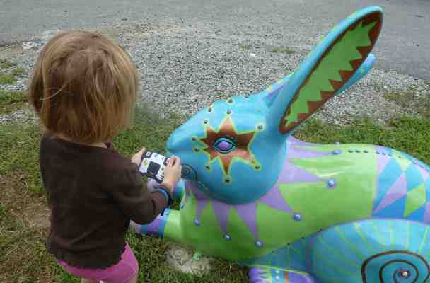 A five-year-old crouches slightly as she takes a picture of a giant rabbit's eye.