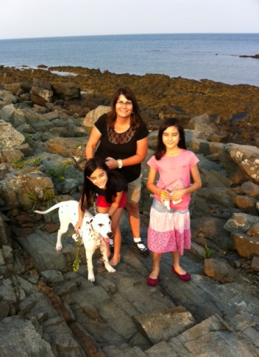 Cathy, her two daughters, and their dog Trooper stand on a rocky beach.