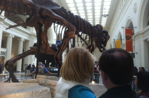 A father holds his daughter as they look at the T. Rex skeleton in the Field Museum.