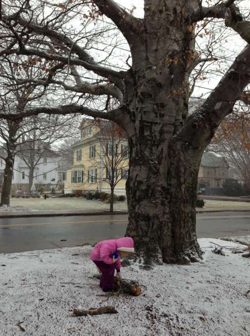 A girl bends over a branch on the ground. There is almost no snow to be seen. 