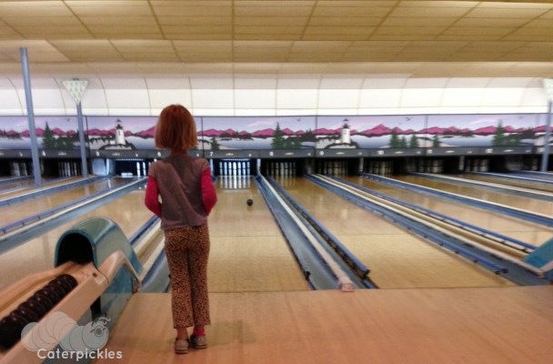 A six-year-old girl watches her bowling ball roll down a candlepin lane.