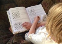 A six-year-old girl reads a book on how to play chess.