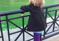 My daughter stands at a black gate overlooking the temporarily bright green Chicago River.