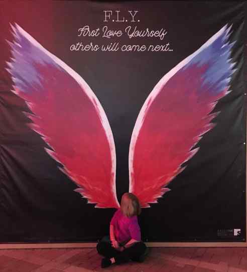 The Ten-Year-Old sits at the base of a giant set of pink wings painted on a wall, so that it looks like the wings are coming out of her back. 
