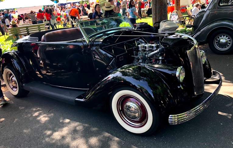 Highly polished black convertible car with smooth lines, a rubber side board to help folks step into the car, leather seats, and white wall tires. Simply lovely. Even if I'm not quite sure what it is. 