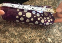 a purple bottle with silver polka dots lies on its side. a measuring tape is stretched across its length.