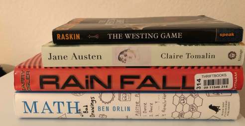 A pile of four books: The Westing Game by Ellen Raskin, Jane Austen by Claire Tomalin, Rainfall by Barry Eisler, and Math with Bad Drawings by Ben Orlin
