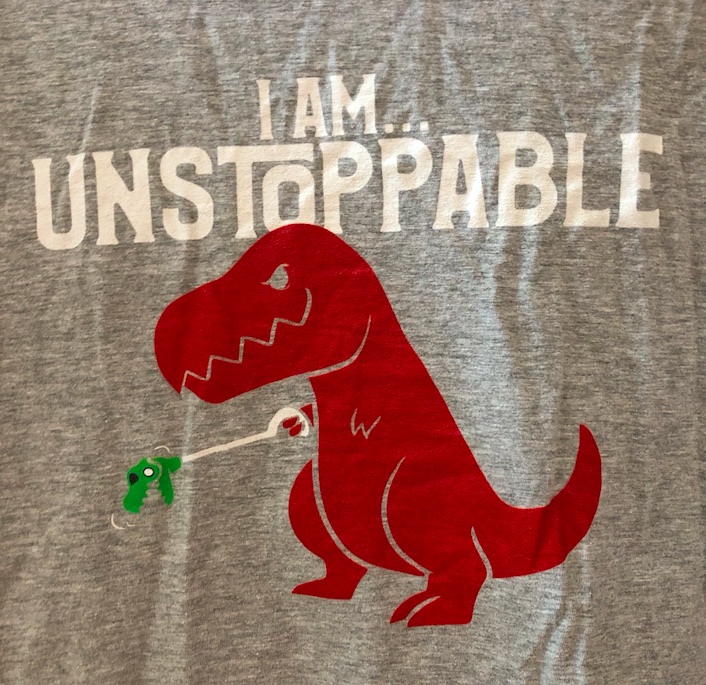 Grey t-shirt with the words "I am unstoppable" above a T. Rex holding one of those mini T. rex grabby toys. 