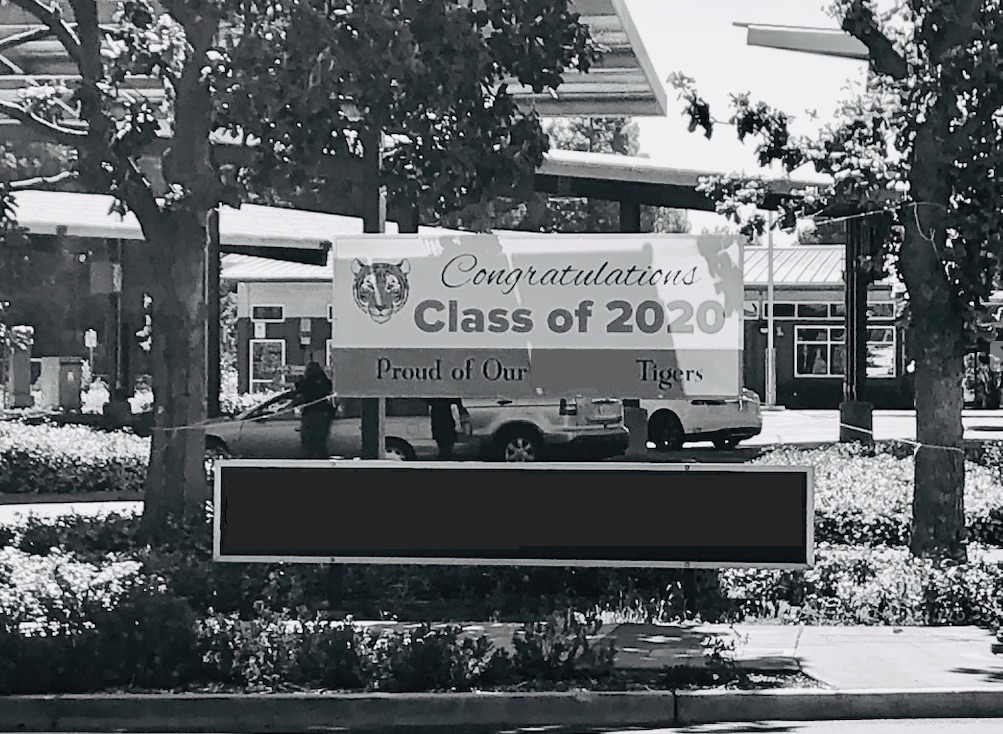 Black and white photo of a banner posted in front of a middle school. Banner reads: "Congratulations Class of 2020: Proud of our Tigers!"