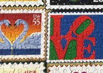 close-up of two stamps from the Love Stamp Puzzle. One shows a pair of swans in profile against a sunset (the swan's necks make a heart). The other shows the LOVE sculpture American artist Robert Indiana which has the letters L and O mounted on top of the V and E.
