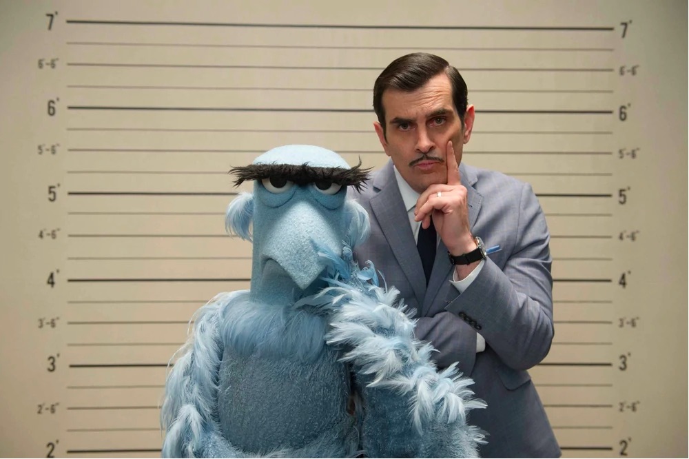 Sam and Jean Pierre Napoleon pose in front of a suspect height wall chart in this still from Muppets Most Wanted. 
