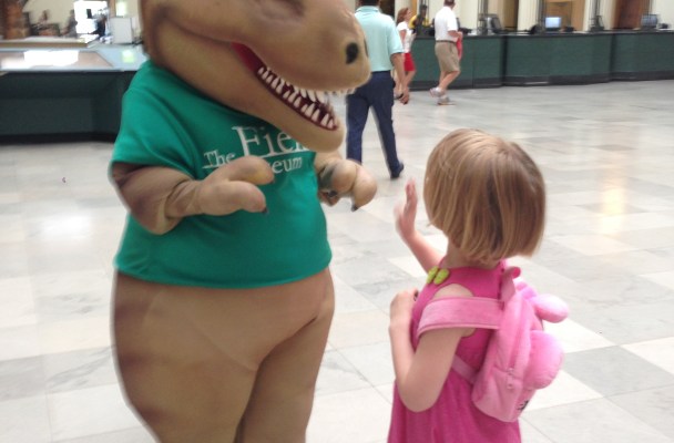 A young girl highfives a museum worker in a t-Rex costume