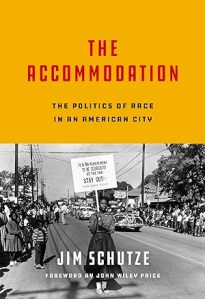 Book cover for the Accommodation by Jim Schutze. The title of the book is set in red against a yellow background on the top half of the book cover. The bottom half shows a black and white photograph of a protest in which Black residents demanded the right to attend the State Fair of Texas. 