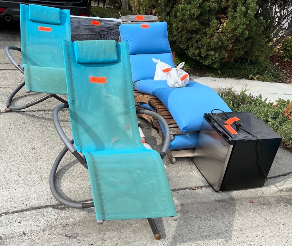 Old yard furniture and a small office-size refrigerator on a curb waiting for pickup. 